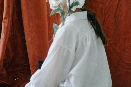 Effortless Chic - Side view of unrecognizable young female in elegant clothes sitting in vintage studio and covering face with bunch of delicate white flowers